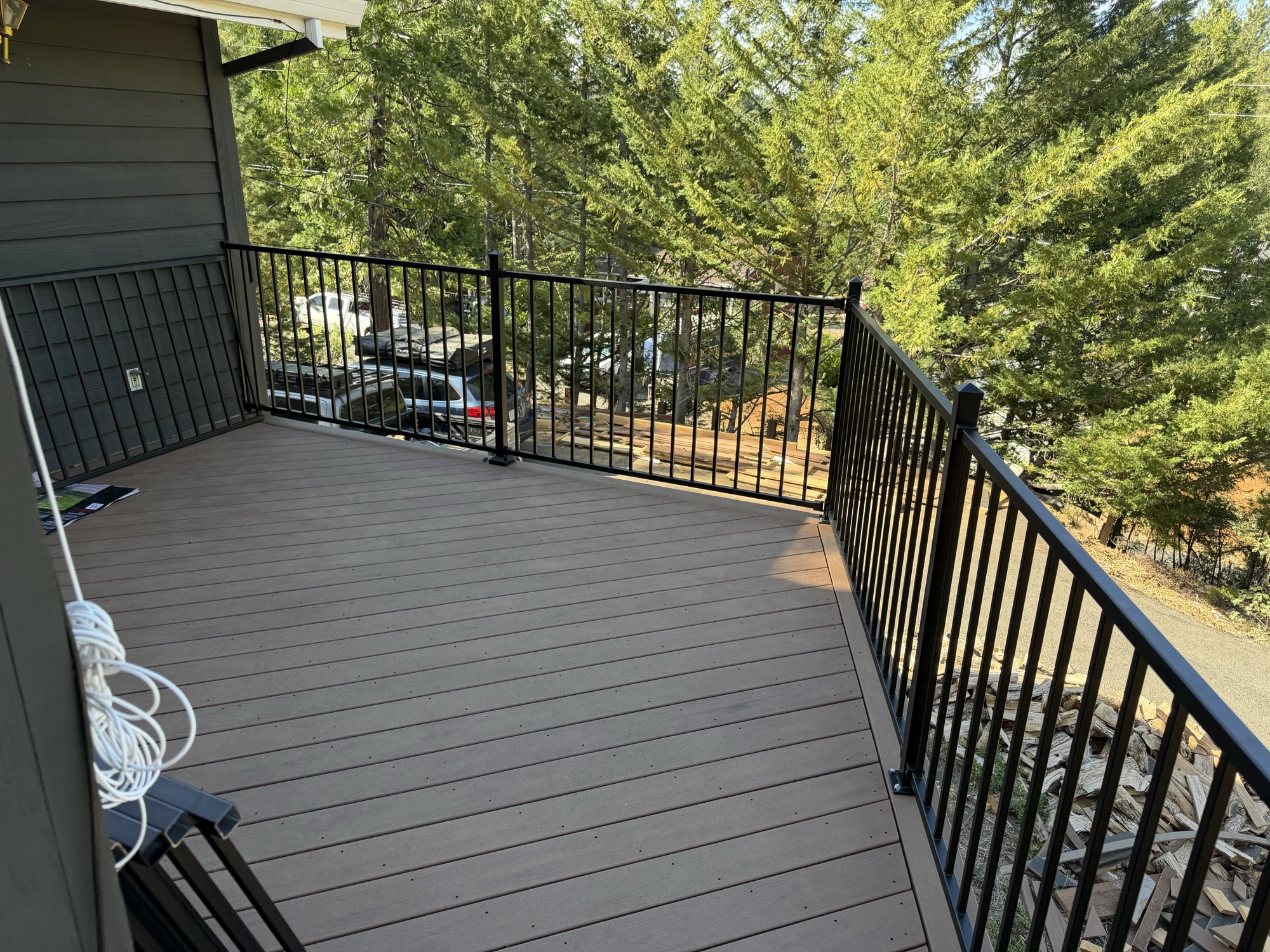 Brown deck surface with black metal picket railing overlooking the trees