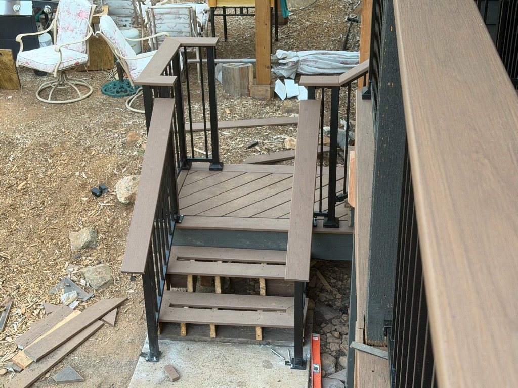 Deck stairs and angled landing with brown decking and black metal picket railing