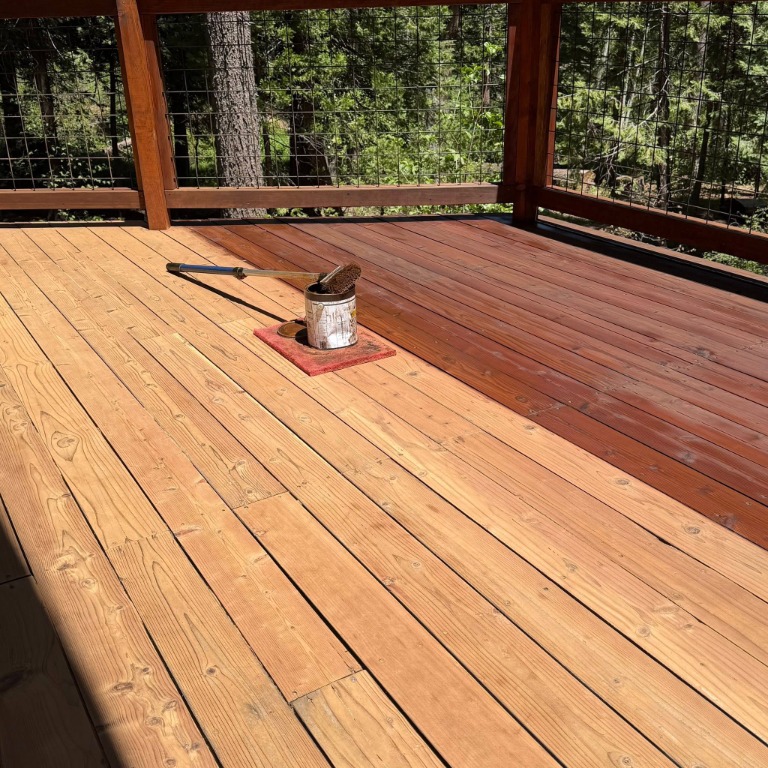 Redwood deck boards being resealed beside a wood and mesh railing